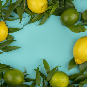 top view of fresh green and yellow lemons with leaves on blue background with copy space
