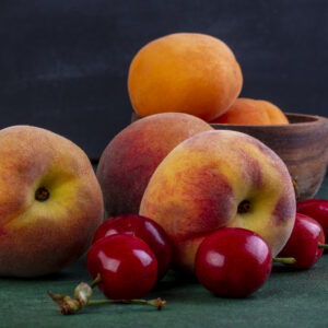 front view peaches with cherries and apricots in a bowl on a green background